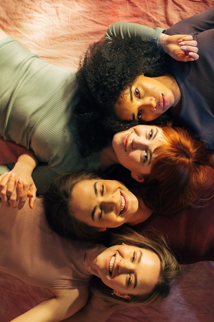 Portrait of four diverse women lying down together smiling warmly at the camera.